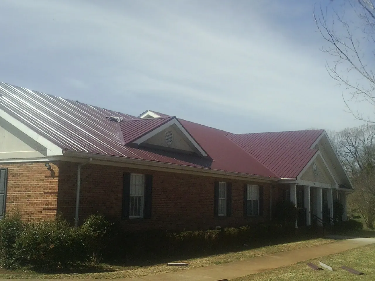 Red metal roof with gabled entries on a long brick building, from a Hail Damage Roof Repair job in Bejou