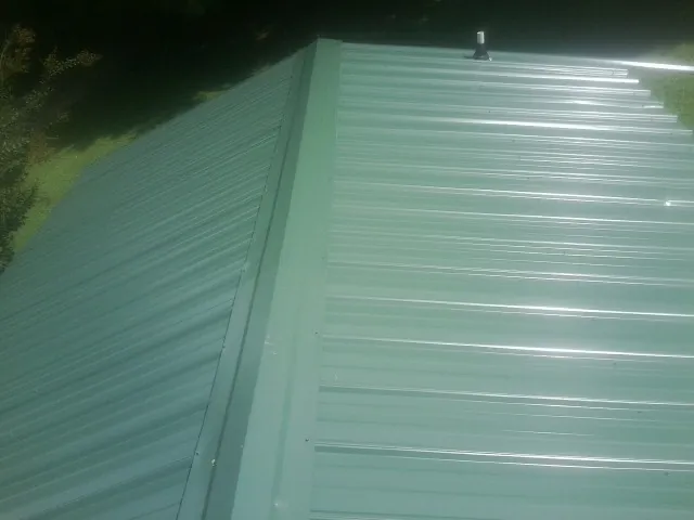 New green metal panels meeting at the ridge of a roof — Flat Roof Repair work by our crew in Bejou