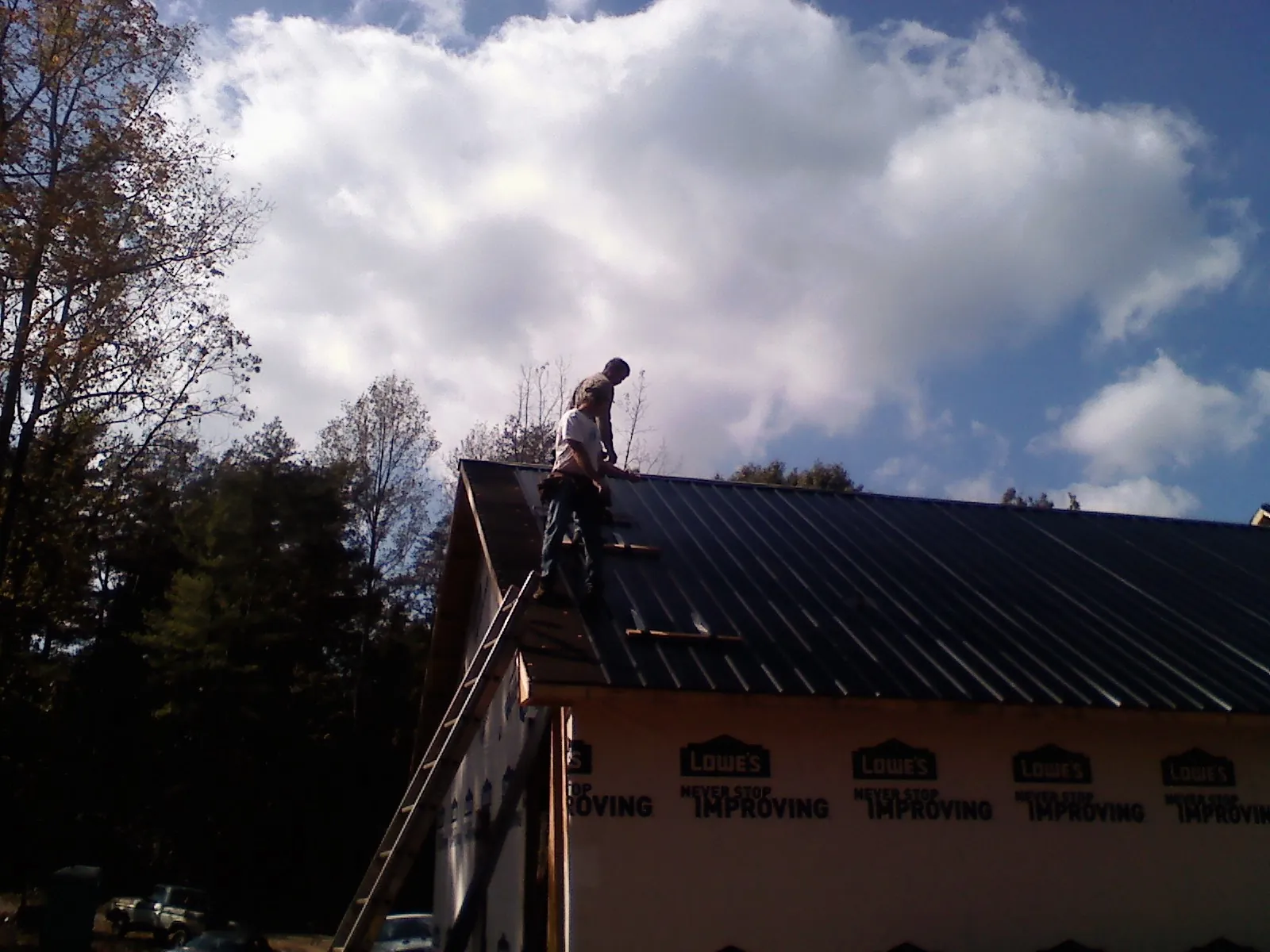 Roofer fastening dark metal panels high against a cloudy sky, from a Roof Inspection job in Bejou