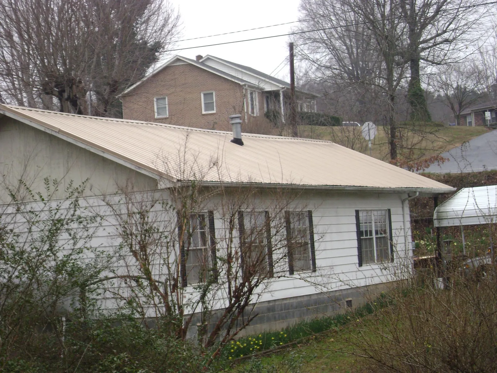 Tan metal roof on a white sided house set into a hillside — Commercial Roofing by Roofing Brothers in Bejou